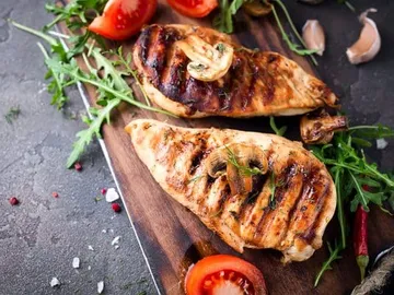 Grilled chicken breast pieces on a wooden board with side dishes.