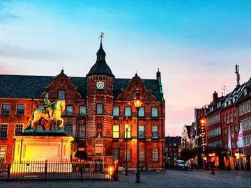 Equestrian statue stands in front of historic buildings with street lamps.
