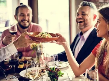 Ein Kellner reicht Pasta an eine lächelnde Frau am Tisch.