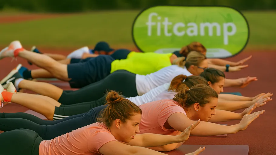 People exercising outdoors on yoga mats, fitcamp sign.