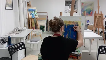 Person malt im Kunststudio mit Staffeleien.