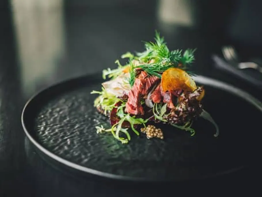 Ein Gericht mit Fleisch und Salat auf schwarzem Teller.