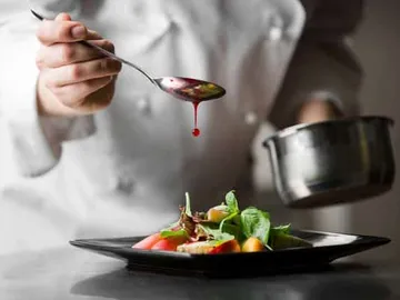 Koch träufelt Sauce über frischen Salat auf Teller.
