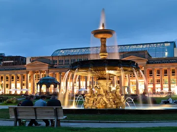 Brunnen sprudelt, während Menschen auf einer Bank sitzen.