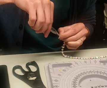 Person fädelt Perlen mit Zange am Tisch.