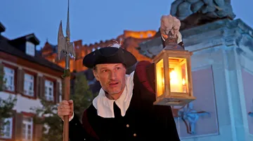 Mann mit Laterne, steht bei Burg in der Dämmerung.