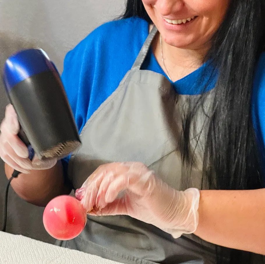 Woman using hairdryer on small red object.