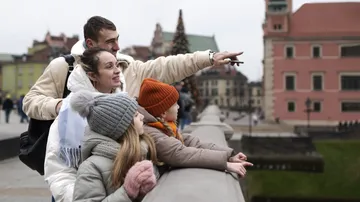 Familie auf Brücke zeigt auf Stadtgebäude.