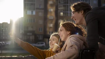 Three friends taking selfie, city backdrop.