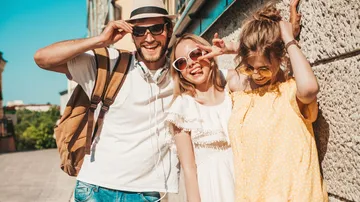 Three friends smiling in sunlight, outdoor city setting.