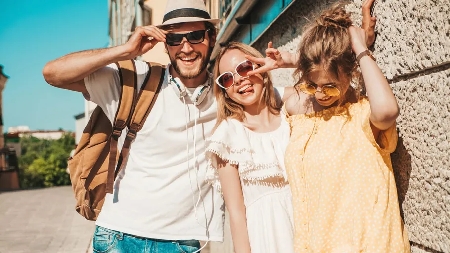 Three friends smiling in sunlight, outdoor city setting.