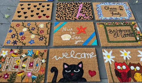 Colorful doormats displayed on a sidewalk.