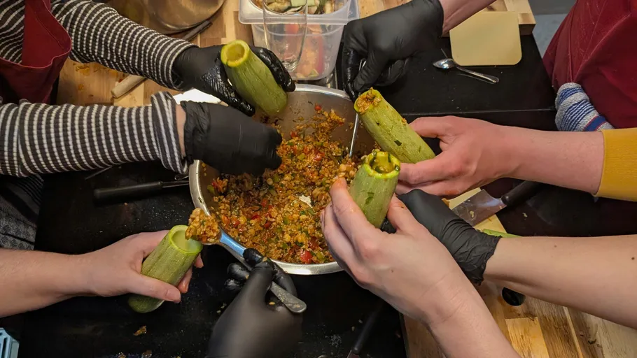 Hands stuffing zucchini with vegetable mixture.