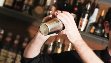 Bartender shakes cocktail shaker behind bar.