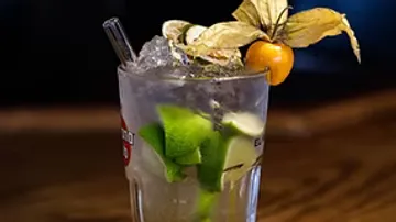 Cocktail with lime and physalis garnish, wooden surface.