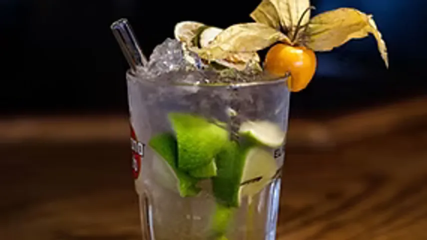 Cocktail mit Limette und Physalis-Garnitur, Holzoberfläche.