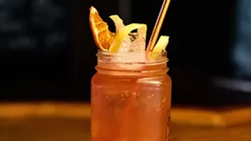 Rosa Cocktail mit Strohhalm und Zitrusgarnitur.