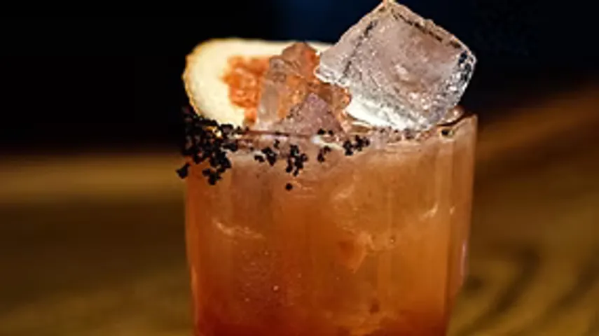 Cocktail mit Eis und Grapefruitstücke auf Tisch.