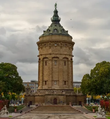 Runder Wasserturm steht im Park unter bewölktem Himmel.
