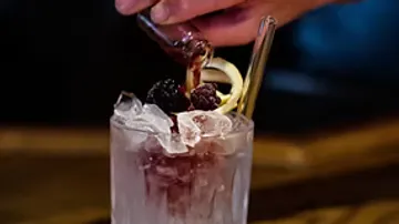 Hand gießt Flüssigkeit in eisgefüllten Cocktail.
