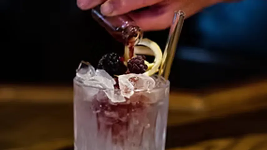 Hand gießt Flüssigkeit in eisgefüllten Cocktail.