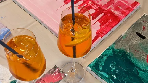 Cocktails with orange slices beside abstract paintings.