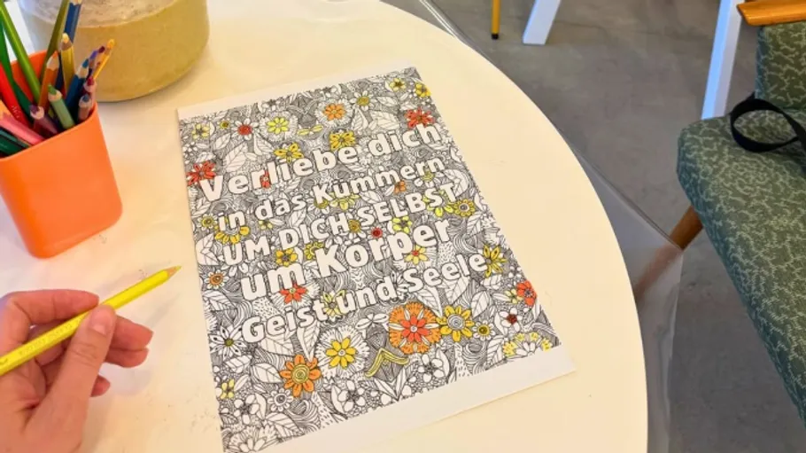 Coloring page on table with pencils, hand holding pencil.