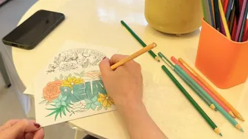 Hand färbt Bild mit Stiften auf Tisch.