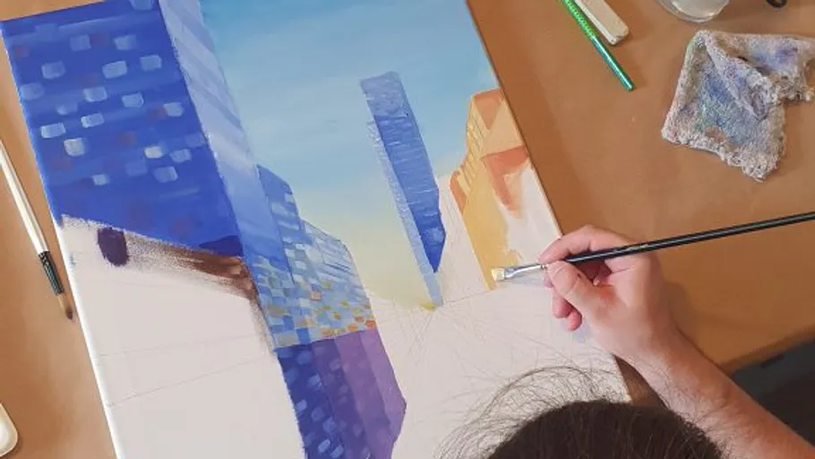 Person painting cityscape on canvas indoors.