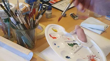 Hand hält Pinsel nahe Farbpalette.
