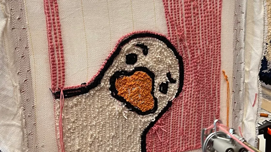 Gestickte Ente auf Stoff mit rosa Hintergrund.