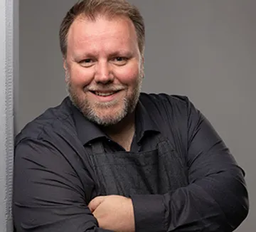 Smiling man with arms crossed, grey background.