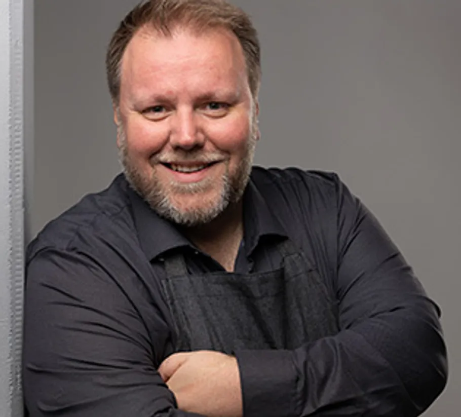 Smiling man with arms crossed, grey background.