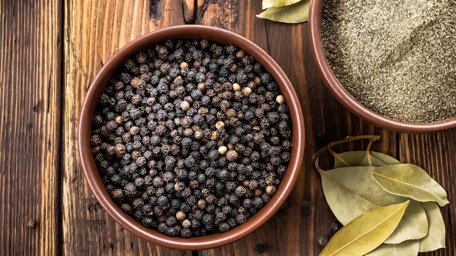 Black peppercorns and ground pepper with bay leaves.