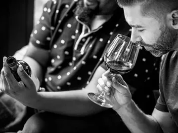 Zwei Männer genießen Wein, einer riecht daran. Gemütliche Atmosphäre.