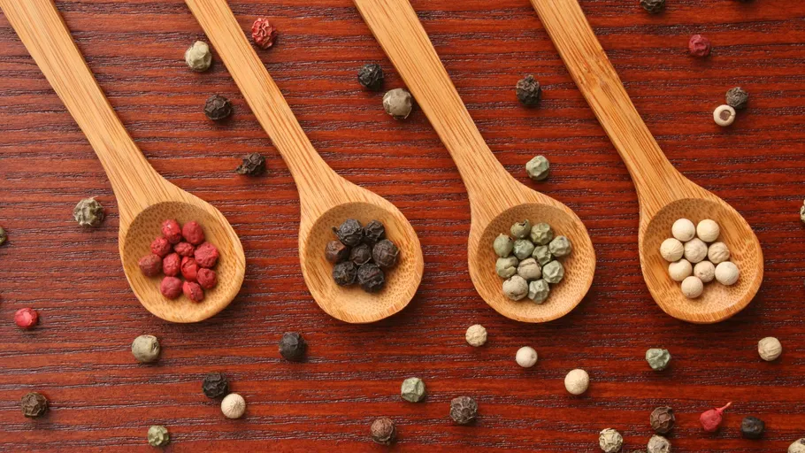 Wooden spoons with colorful peppercorns on table.