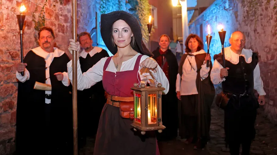 Personen in historischer Kleidung mit Laternen und Fackeln.