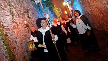 Gruppe in historischen Kleidern mit Fackeln, Gassenszene.