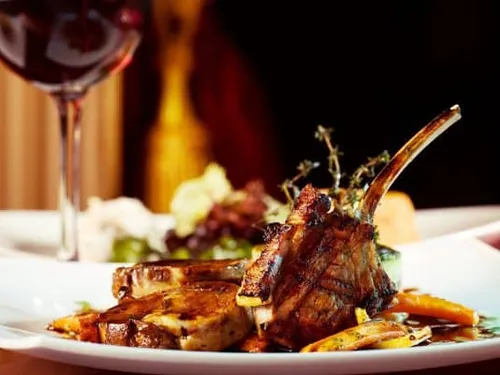 Grilled meat is placed on a plate next to red wine.