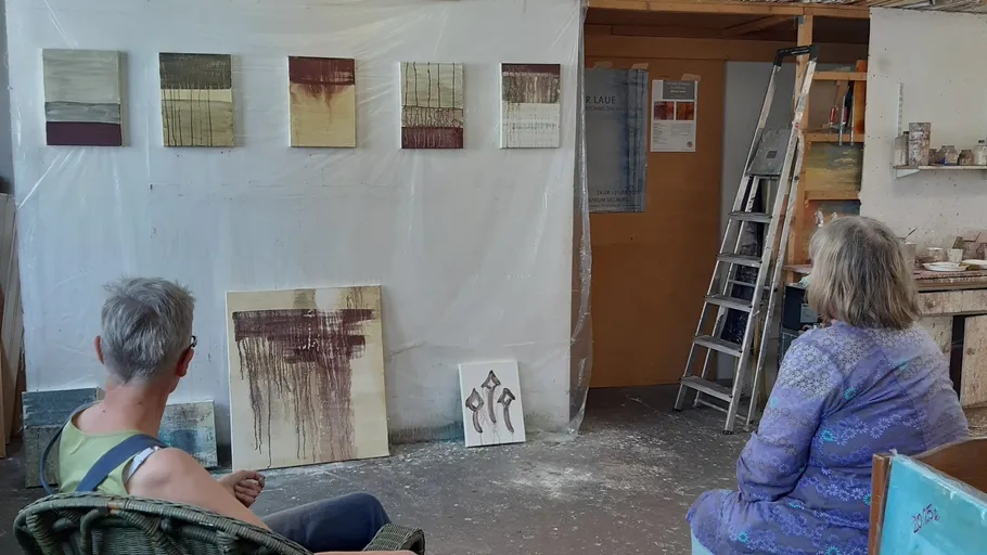 Two people observing abstract paintings in a studio.