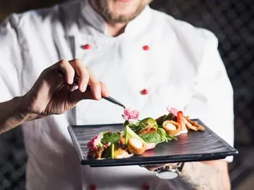 Cook carefully decorates a dish on a black plate.