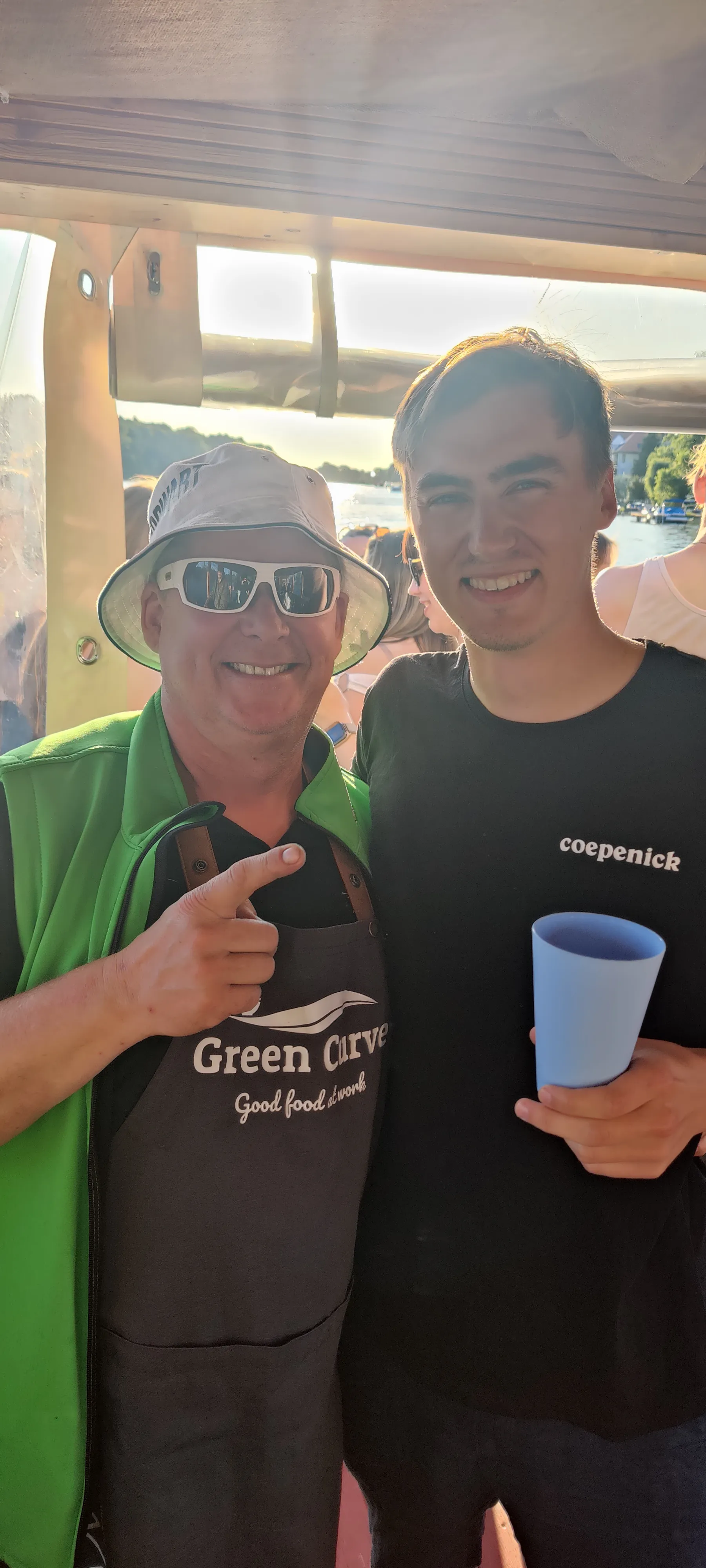 Zwei Männer lächeln auf einem Boot im Sonnenlicht.