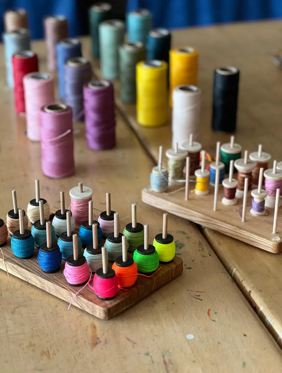 Colorful thread spools arranged on wooden holders.