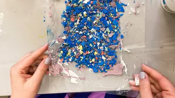 Hände halten bunte Plastikscherben auf Oberfläche.
