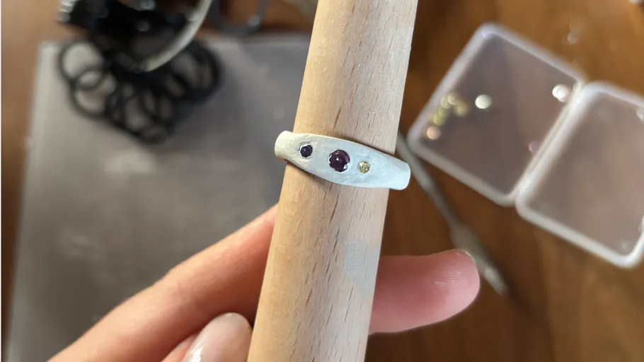 Hand hält Edelsteinring auf Holzdübel.