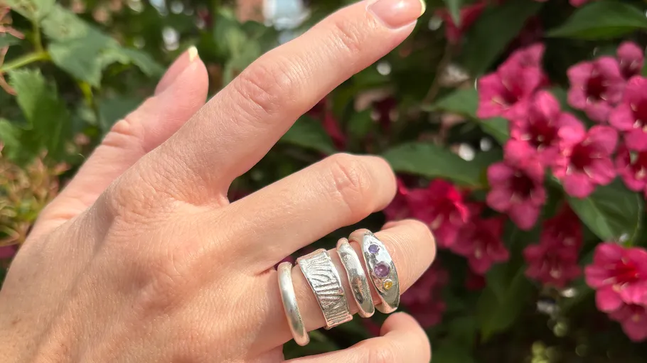 Hand mit Silberringen nahe rosa Blumen.