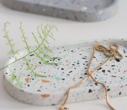 Terrazzo-Tablett mit Schmuck und Pflanzenspross.