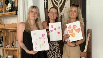Drei Frauen halten Blumenbilder innen.
