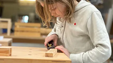 Kind hobelt Holz in einer Werkstatt.
