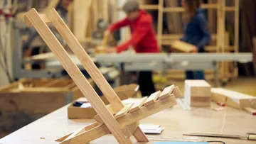 Holzständer auf Tisch, Personen arbeiten im Hintergrund.